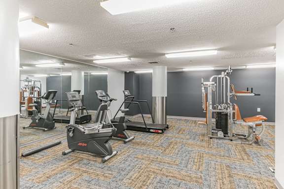 a gym with treadmills and other exercise equipment in a room with gray walls at Mill House Apartments, Greenfield, MA, 01301