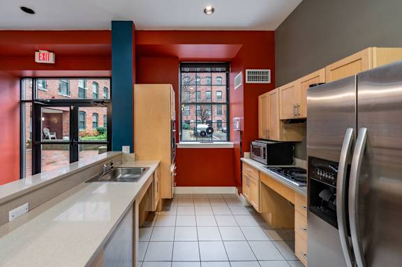 A kitchen with a red wall and a stainless steel refrigerator at The Cordovan at Haverhill Station, Haverhill, Massachusetts