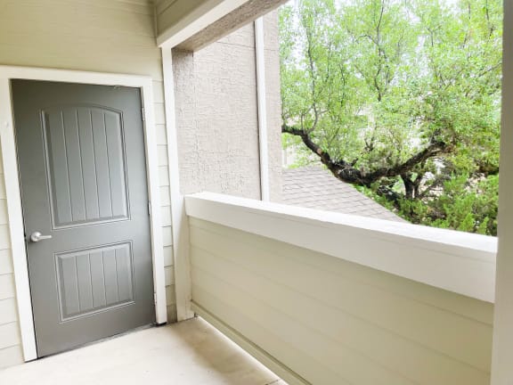 a gray door on a white house with a large window and trees in the background