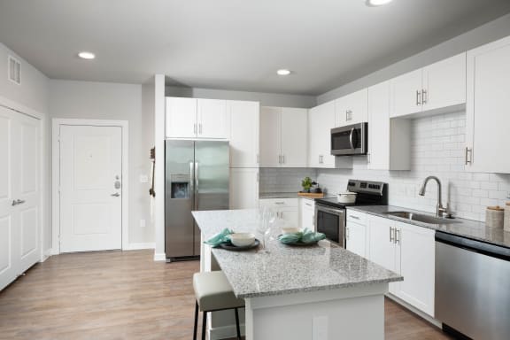 a white kitchen with a granite counter top and stainless steel appliances at 55 Fifty at Northwest Crossing, Houston, 77092