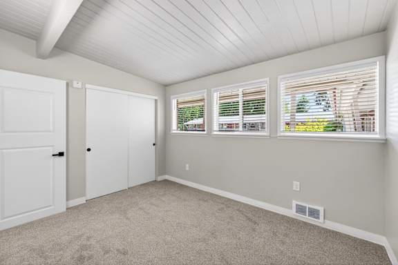 A room with a white ceiling, carpeted floor, and three windows with blinds.