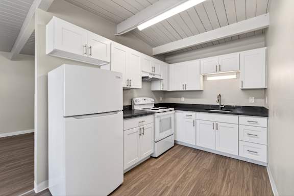 A white refrigerator is in a kitchen with white cabinets and a black counter.