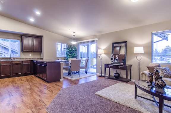 A well-lit living room with a brown wooden floor and furniture.