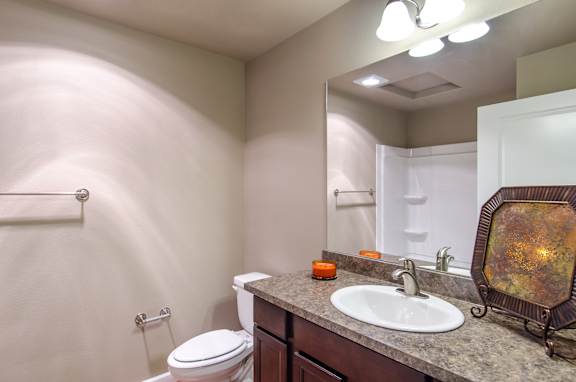 A bathroom with a toilet, sink, mirror, and towel rack.