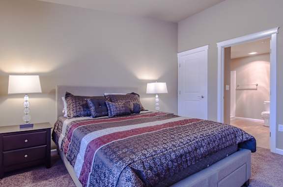 A bedroom with a large bed and two lamps.