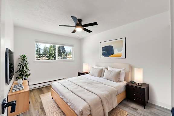 A bedroom with a large bed, a ceiling fan, and a window with a view of trees.