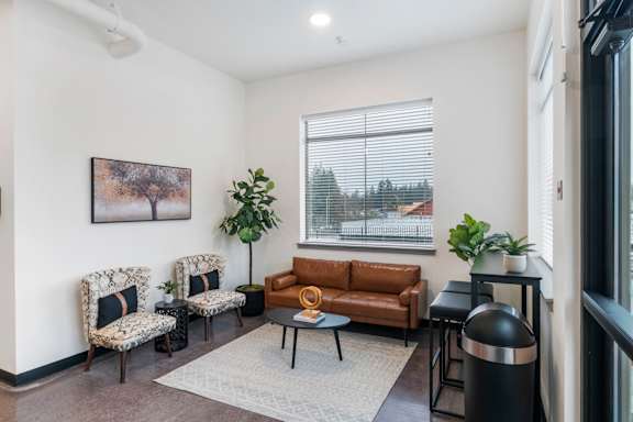 A living room with a brown couch, two chairs, a coffee table, and a plant.