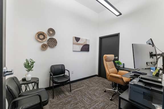 A room with a desk, chairs, and a plant.