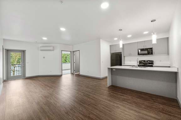 A spacious living room with a kitchenette and a view of the outdoors through a sliding glass door.