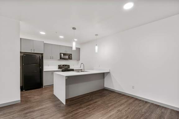 A modern kitchen with a black refrigerator and wooden floors.