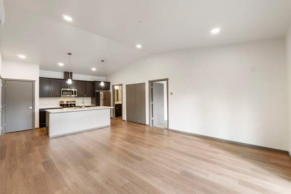 A spacious room with wooden flooring and a kitchen area in the background.