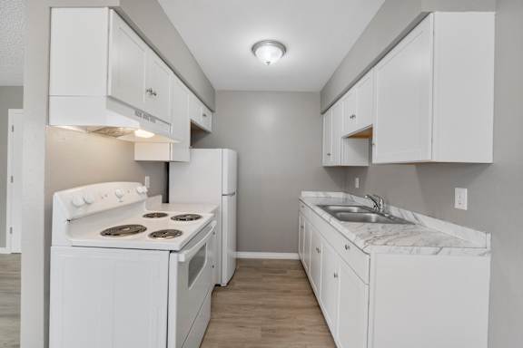 A white kitchen with a stove, sink, and cabinets.