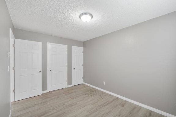 A room with three white doors and wooden flooring.