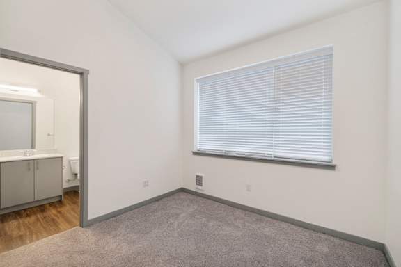 A room with a carpeted floor and a window with blinds.