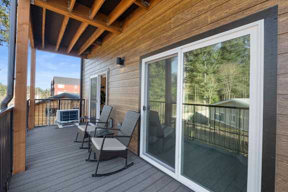 A wooden deck with two chairs and a sliding glass door.