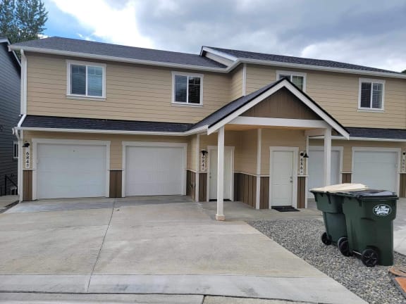 a beige house with white garage doors and a gravel driveway
