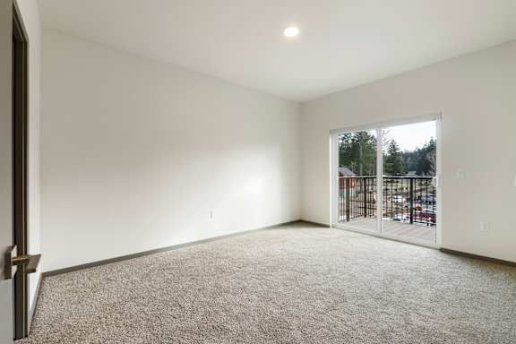 A room with a carpeted floor and a sliding glass door leading to a parking lot.