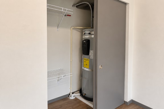 A small, white refrigerator is in a narrow space next to a wall.