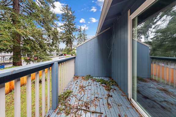 A deck with a railing and a view of trees and a fence.