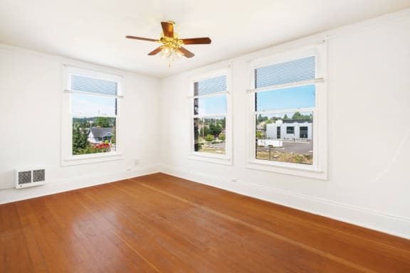 an empty living room with a ceiling fan and three windows