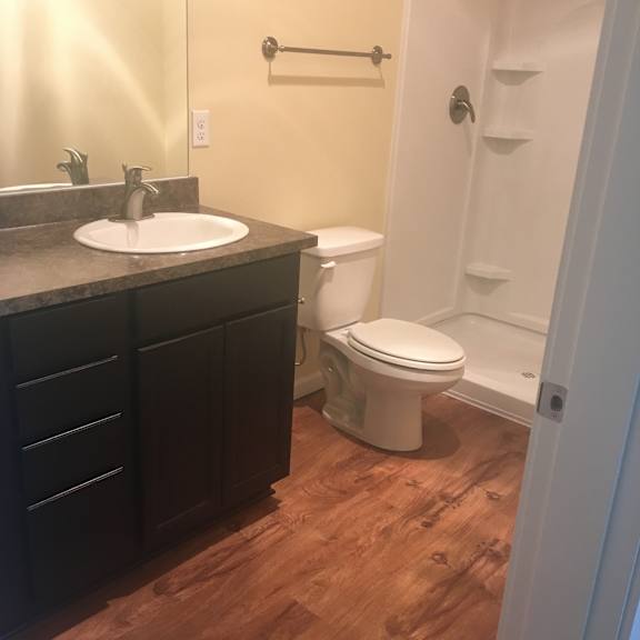 A white toilet is in a bathroom with wood flooring.