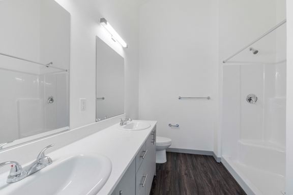 A white bathroom with a sink, mirror, toilet, and shower.