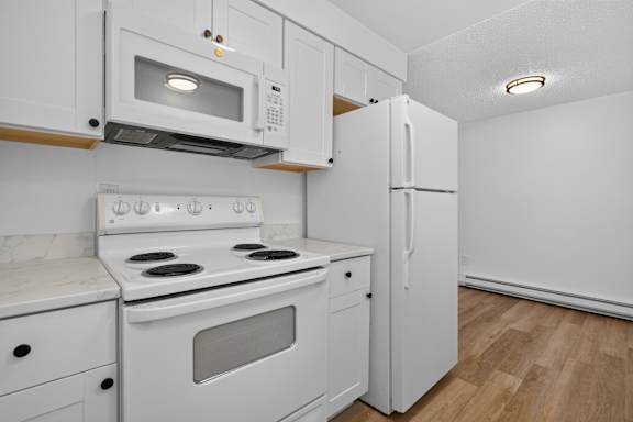 A white kitchen with a stove, microwave, and refrigerator.
