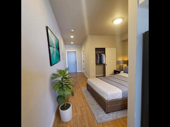A bedroom with a bed, a plant, and a painting on the wall.