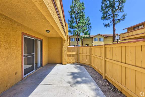 A yellow house with a wooden fence and a tree in the background.