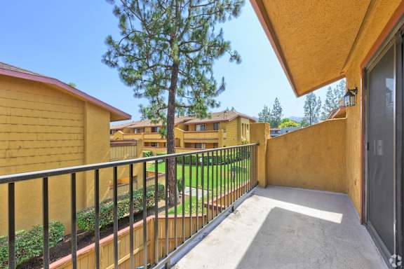 A balcony with a black railing and a tree in the background.