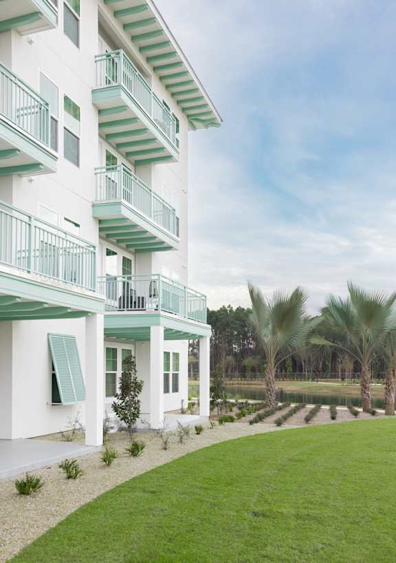 A white building with green balconies and a green lawn in front.
