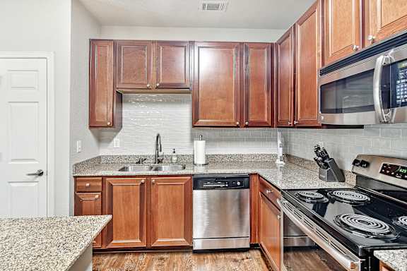 Kitchen with wooden cabinets and a granite countertop and stainless steel dishwasher at Faulkner Flats Apartment Homes, Mississippi