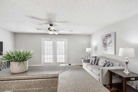 A living room with a grey couch, a plant, and a painting on the wall at The Pointe Apartment Homes in Gautier, MS