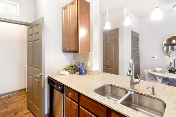 a kitchen with a dishwasher, sink and a quartz counter top with wooden cabinets  at Kingston Crossing Apartment Homes, Bossier City, Louisiana