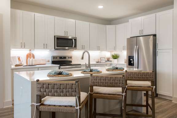 A kitchen with a refrigerator, microwave, and two chairs.