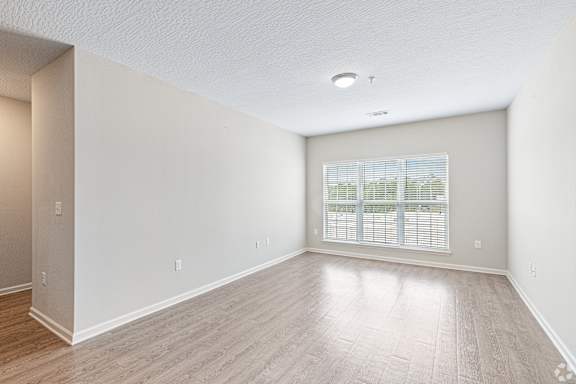 an empty living room with a large window and wood flooring at The Met Apartment Homes, Hattiesburg