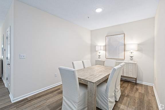 a dining room with a wooden table and white chairs at The Met Apartment Homes, Hattiesburg