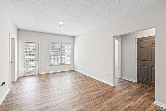 an empty living room with wood flooring and a brown door at The Met Apartment Homes, Mississippi 39402