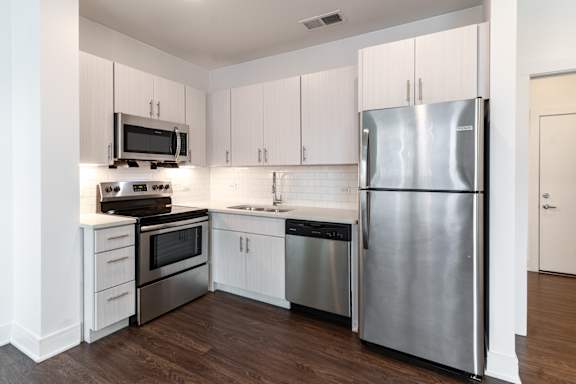 A modern kitchen with a stainless steel refrigerator, microwave, oven, and sink. at The Whit Apartments, Indianapolis, 46204