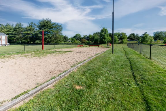 a sand volleyball court in a park with a fence and grass