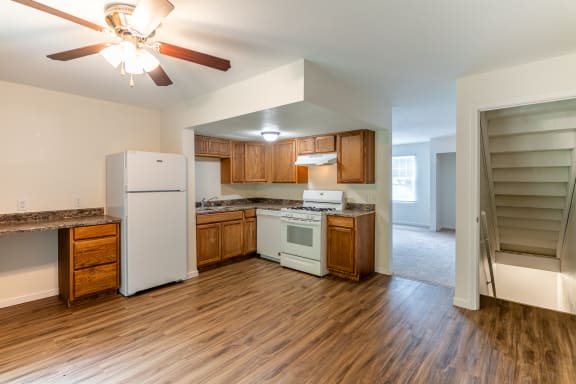 an empty kitchen with white appliances and wooden floors