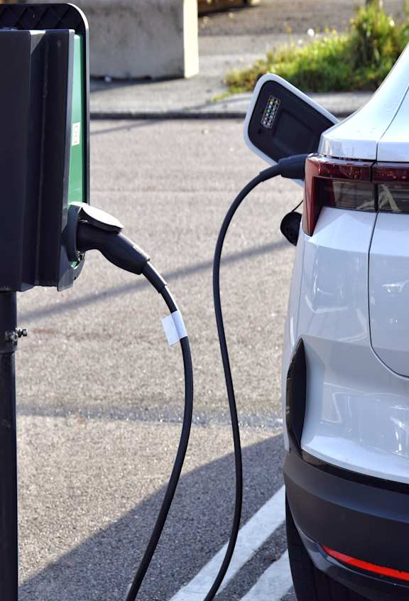 A white car is charging at a black charging station.