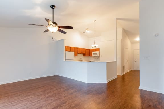 an empty living room with a ceiling fan and a kitchen