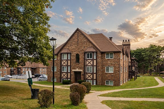 A large brick building with a triangular roof and a small tower is surrounded by a grassy area and trees.