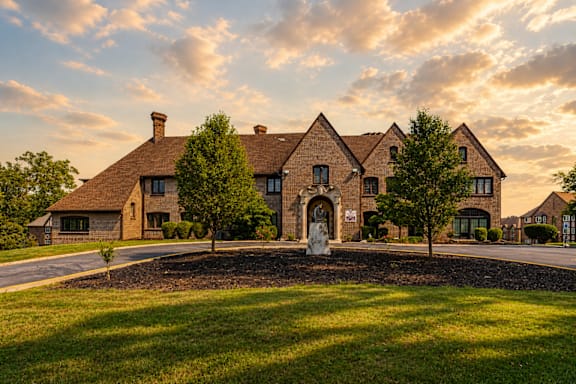 A large house with a driveway and a fountain in front.