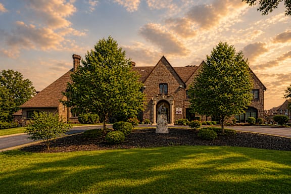 A large house with a stone wall and a large tree in front.