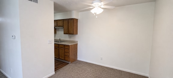 A room with a ceiling fan and a kitchenette.