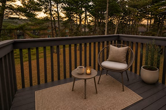 A chair and table set up on a deck with a view of the trees.