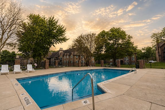 A swimming pool surrounded by trees and chairs.