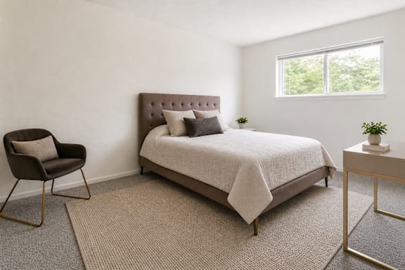 A bedroom with a bed, chair, and nightstand.
